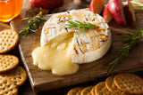 A wheel of melty brie cheese surrounded by crackers and a jar of Clif Family Solar Grown Honey in the background.|Hot Tam Recipe