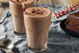 A Chocolate Peanut Butter Milkshake made with Clif Family Solar Grown Cacao Honey Spread in a glass topped with shaved chocolate pieces. This plant-based recipe is available on the Clif Family Winery blog.