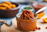 Close-up of Clif Family's Spicy Sundried Tomato Pesto in a clear glass jar, showcasing its vibrant red-orange color, made from Clif Family's made with Organic Hot Honey Cashews & Peanuts.|