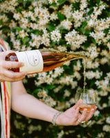 Person pouring rosé wine into a glass with a floral background