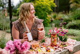 Woman holding a bottle of Clif Family Rose of Grenache surrounded by a beautiful pink garden setup
