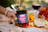Someone holding Clif Family Red Wine Jelly with Cracked pepper in front of a table with charcuterie and wine