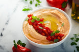 A bowl of Clif Family Spanish Pimenton Almond Miso Spread sits in a bowl garnished with diced red peppers.|A bottle of Clif Family Rose of Grenache sits on table with a poured glass and cheese board. Vineyards are in the background.