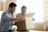 |Happy millennial couple sitting on cozy sofa, unboxing cardboard parcel