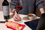 Person holding a glass of red wine in front of a laptop