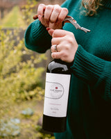 Person opening a bottle of Clif Family Cabernet Franc with a corkscrew outdoors.