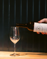 Person pouring wine from a bottle of Clif Family Napa Valley Sauvignon Blanc into a glass against a dark background.