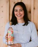 Winemaker, Laura Barrett, holding a bottle of rose wine with a floral label against a wooden background.