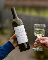 Person holding a bottle and a glass of Clif Family Napa Valley Sauvignon Blanc with a blurred outdoor background