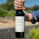 Someone holding a bottle of Cabernet Franc in front of a vineyard