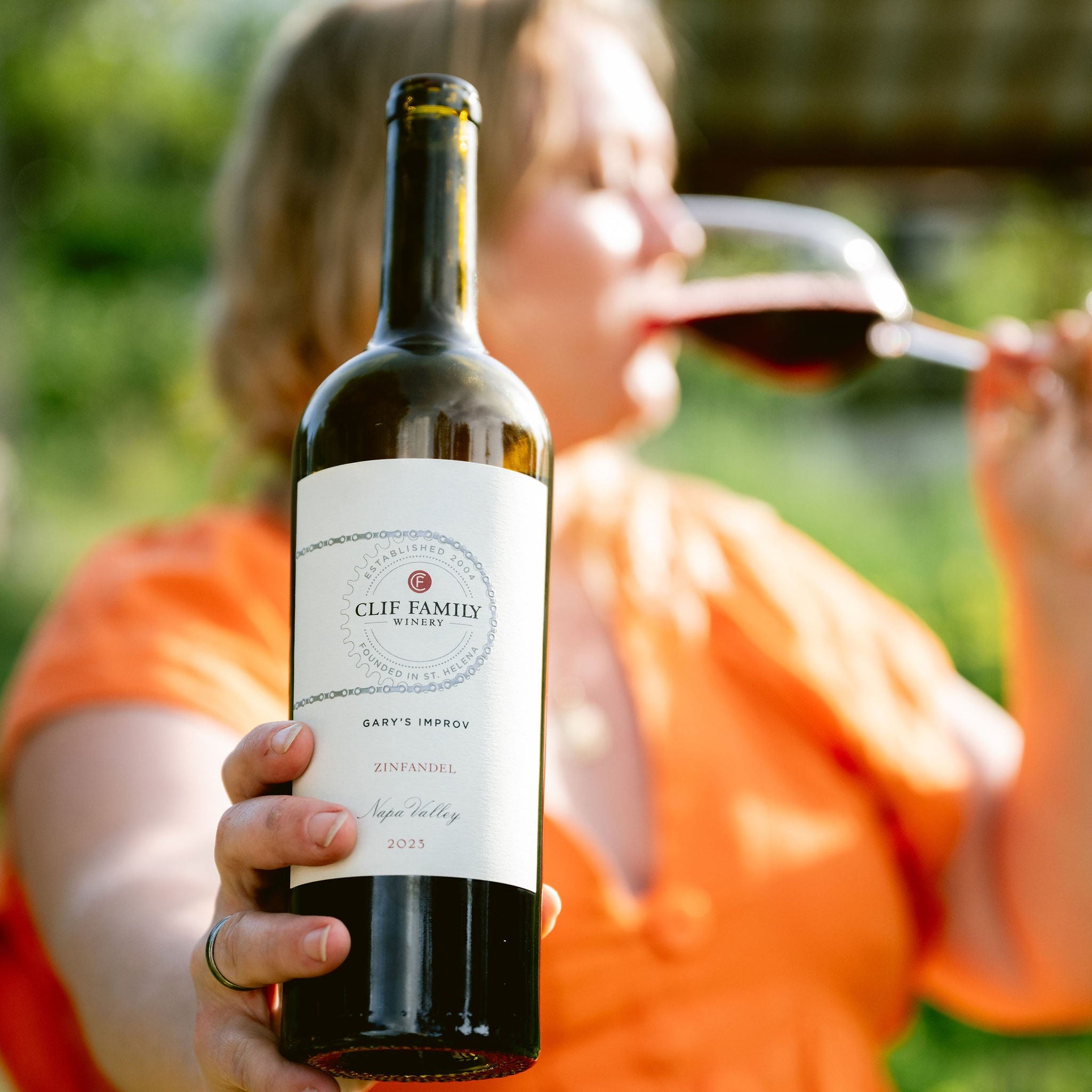 Person holding a bottle of wine with a blurred outdoor background