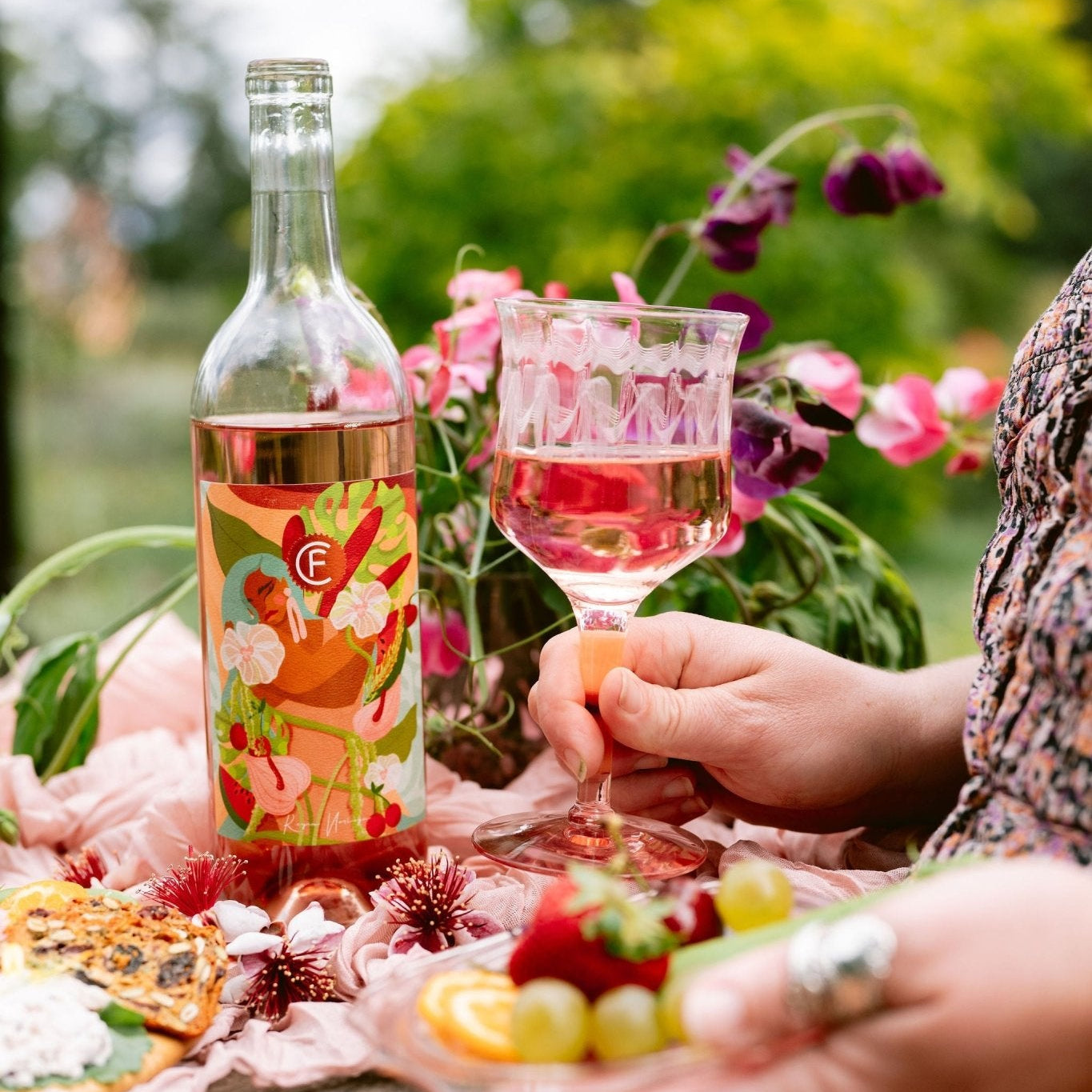 Person holding a glass of 2025 Clif Family x Reyna Noriega Rose of Cabernet Franc and a plate of fruit
