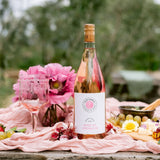 Bottle and glass of 2025 Rosé of Grenache on pink picnic blanket with florals in the background