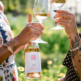 Woman holding bottle and glass of 2025 Rose of Grenache clinking glasses with someone else