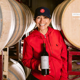 Woman in between rows of wine barrels holding a bottle of wine