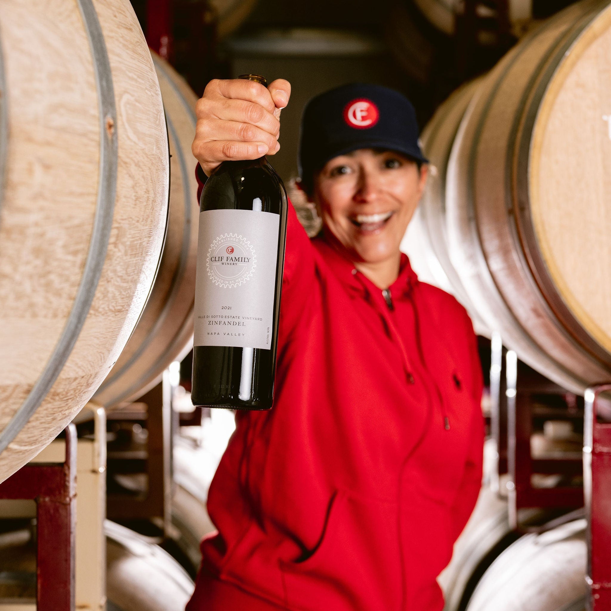 Person holding a bottle of wine in a winery with barrels in the background
