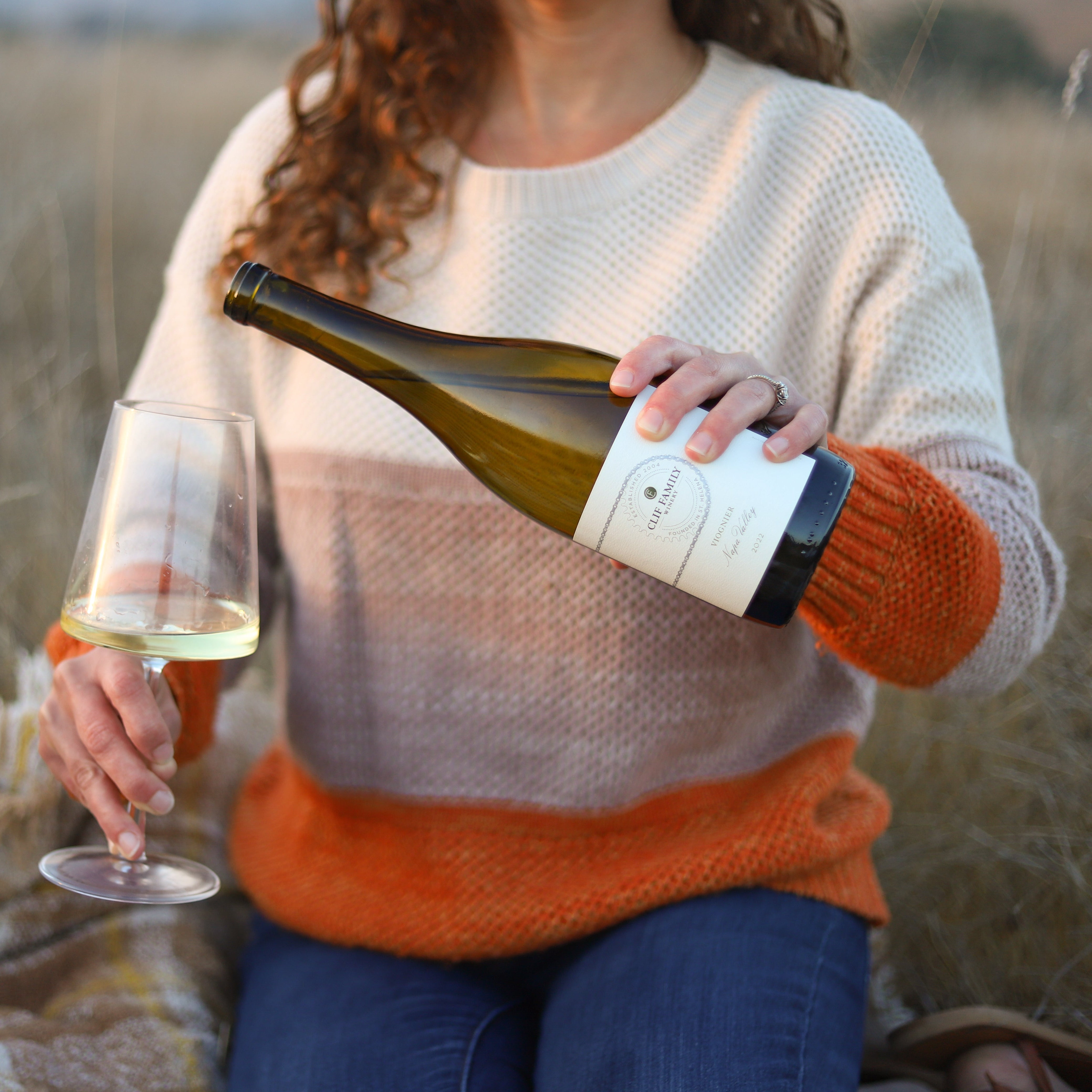 Woman sitting in field pouring a glass of white wine