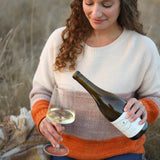 Woman sitting in a field pouring Viognier into a wine glass