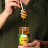 Person using a honey dipper to draw honey from a jar labeled 'Clif Family Solar Grown Raw Honey'.