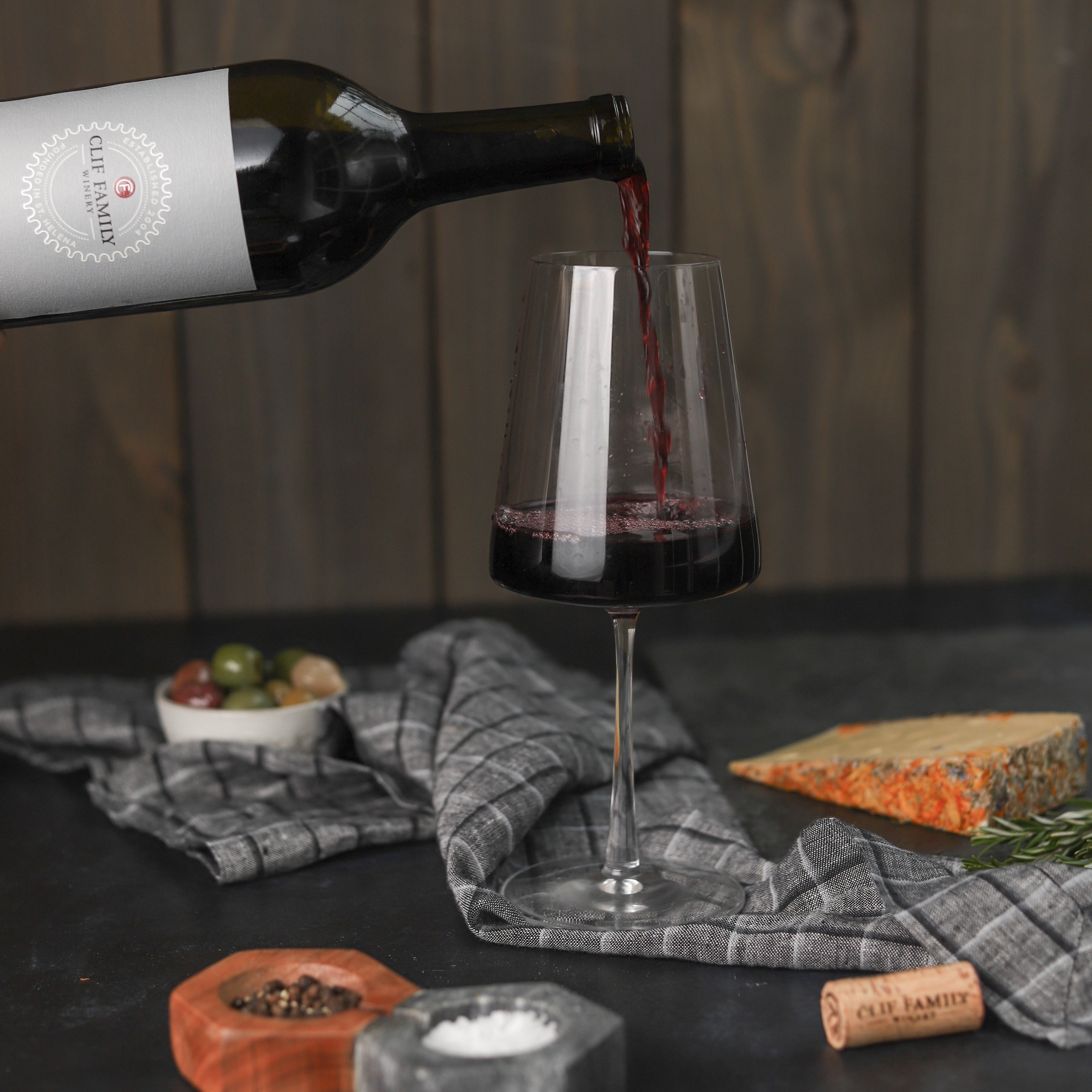 Zinfandel being pouring into a wine glass accompanied by cheese and other accoutrement. 